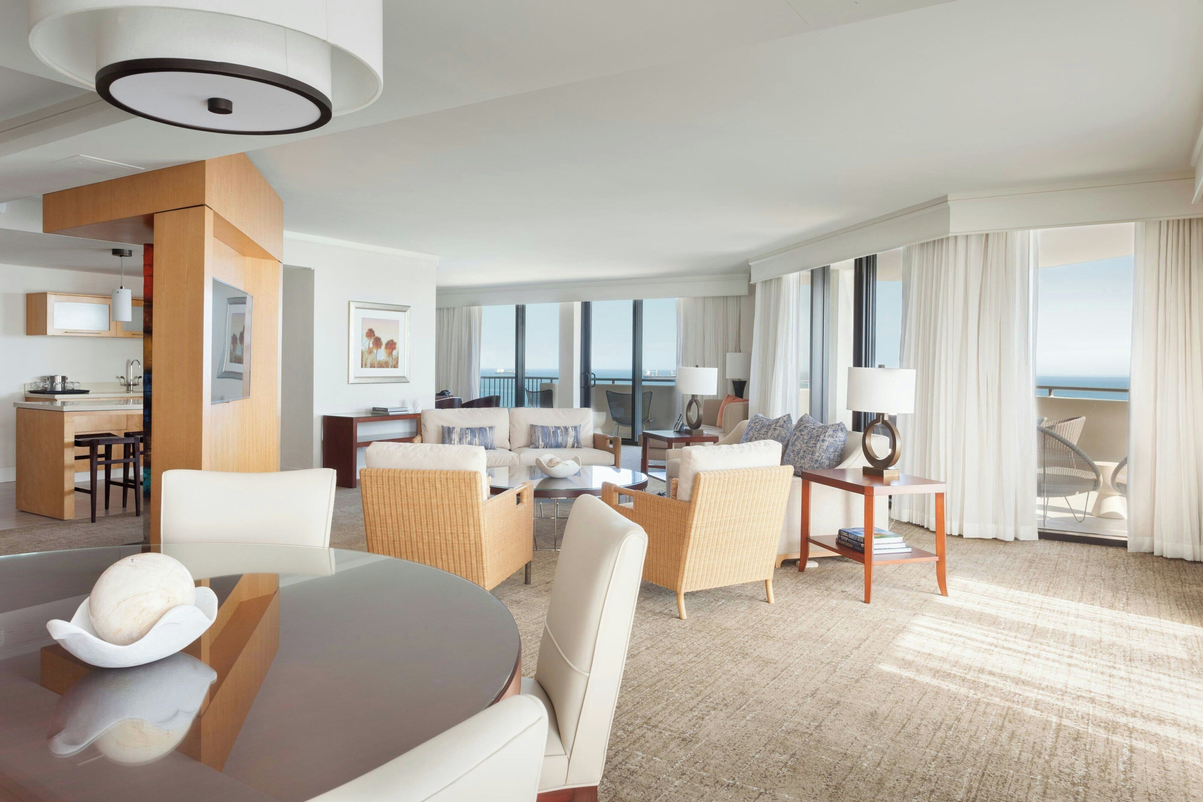 Une chambre d’hôtel moderne dotée d’un coin repas, d’un ensemble de canapés, d’une petite table et offrant une vue sur la mer.
