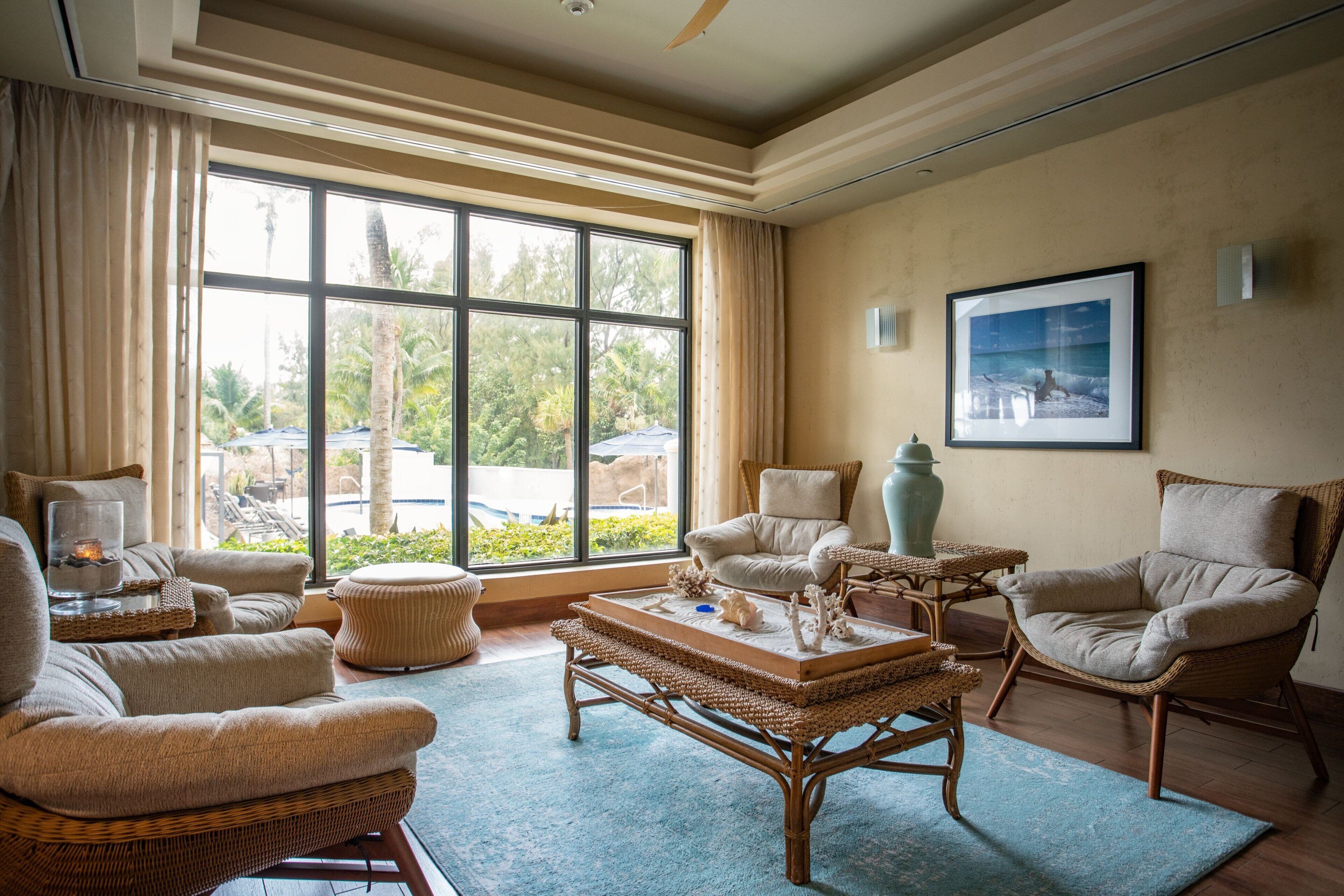 Un salón espacioso con un ventanal grande, mobiliario de mimbre y vistas al exterior.