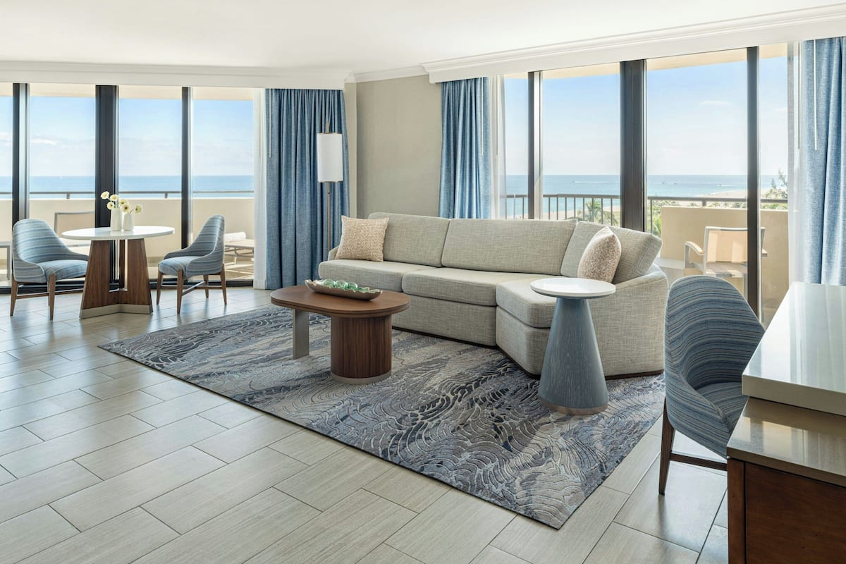 Een moderne hotelkamer met een ruim balkon, een bank, twee fauteuils, een salontafel en een eethoek.