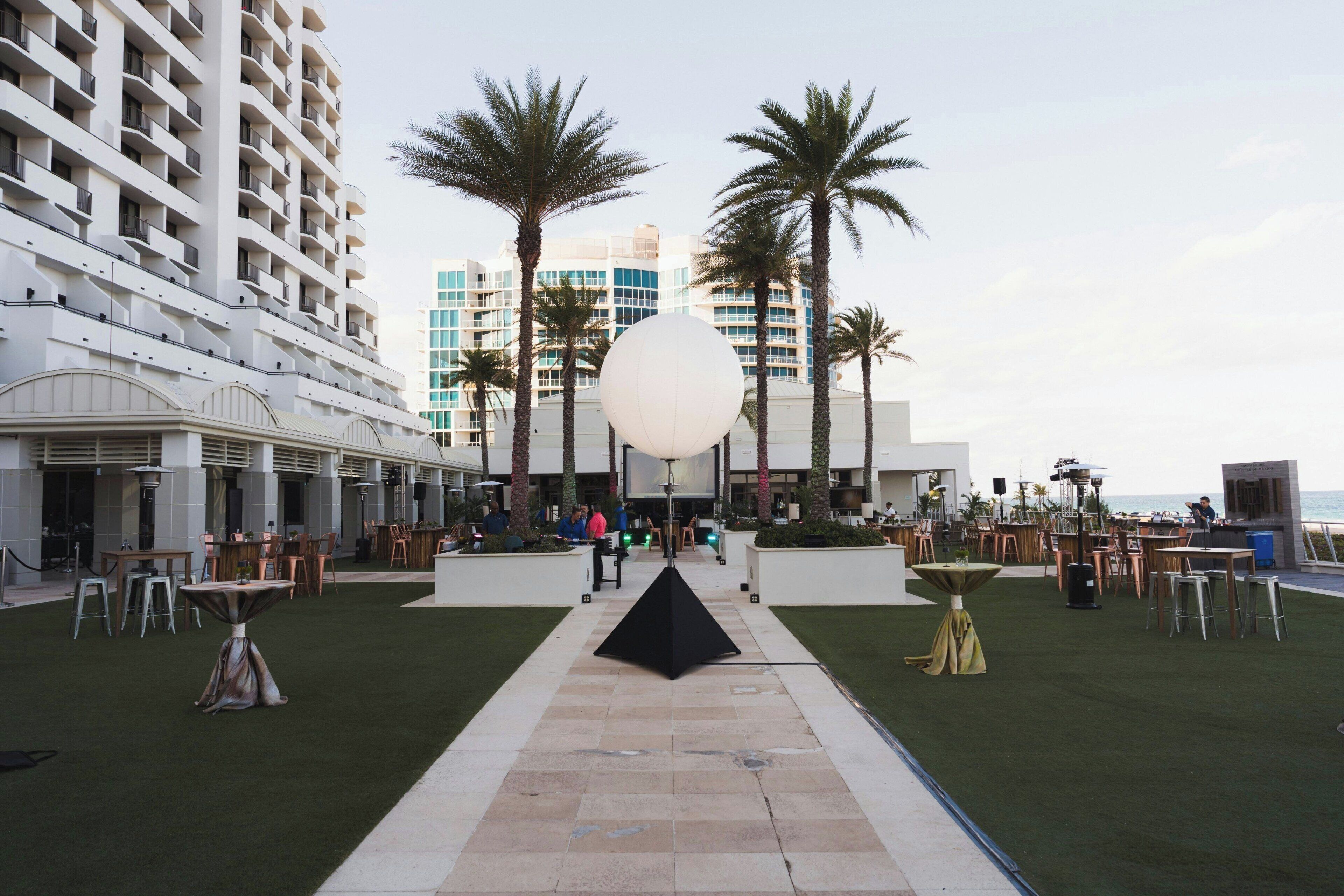 A hotel courtyard with outdoor seating, palm trees, and a large spherical light fixture.