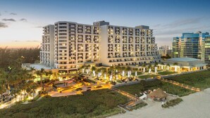 Een meerlaags hotel met een centrale binnenplaats, omringd door palmbomen en uitzicht op het strand.