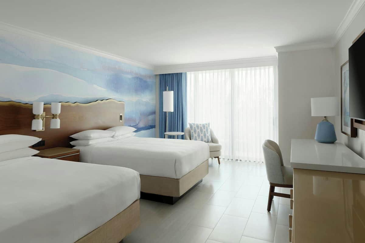 Een hotelkamer met twee bedden, een bureau, een stoel, een televisie en een schilderij aan de muur.