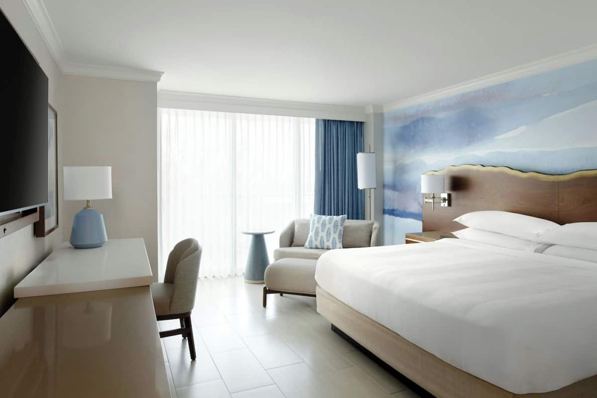 Een hotelkamer met een groot bed, een bureau met een lamp, een stoel en uitzicht op het omliggende landschap.