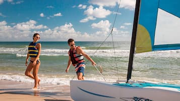 Un velero llamado 'Hobie' en una playa con dos personas usando chalecos salvavidas.