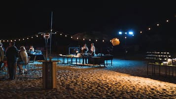 Un espace de restauration en plein air avec des tables et des chaises, des guirlandes lumineuses et une structure en chaume en arrière-plan.