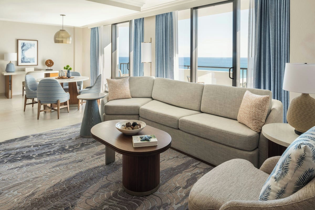 Een moderne woonkamer met een beige modulaire bank, een ronde salontafel, en een eethoek met een kleine tafel en stoelen.