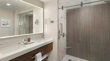 Un baño moderno con un espejo grande, dos lavamanos, una ducha y un mueble de tocador de madera.