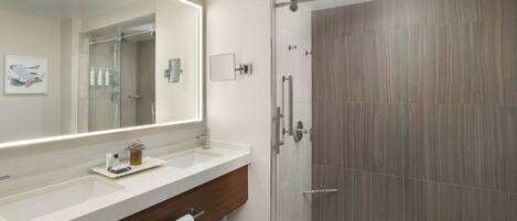 Un baño moderno con un espejo grande, dos lavamanos, una ducha y un mueble de tocador de madera.