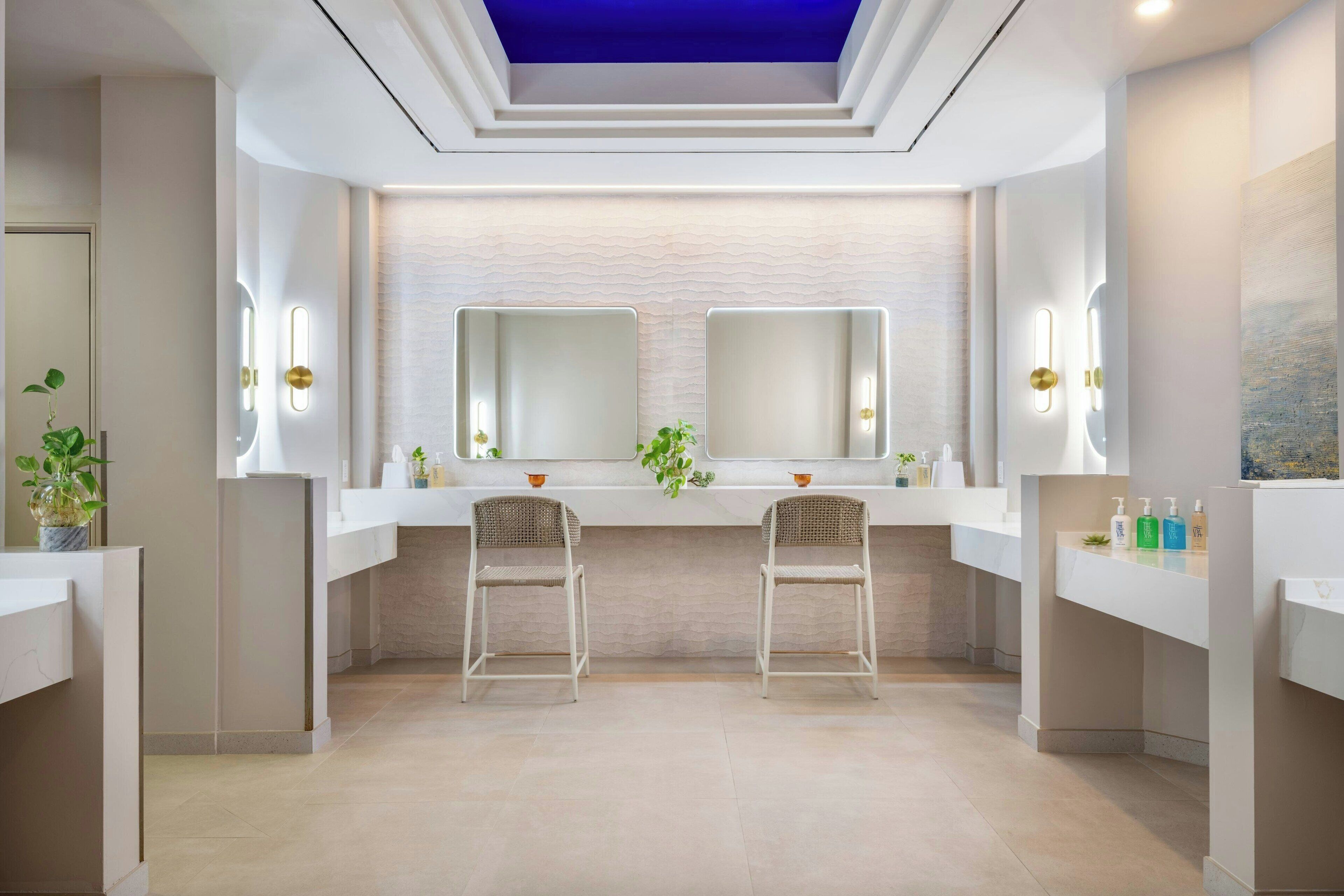 A modern bathroom with two sinks, mirrors, and chairs.