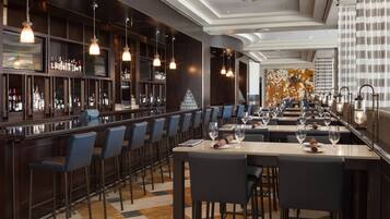 A modern bar area with a long counter, multiple bar stools, and a variety of bottles and glasses.
