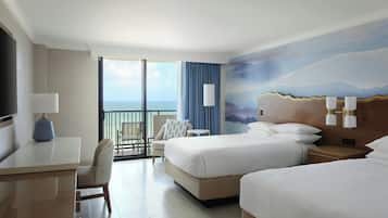 A hotel room with two beds, a desk, a chair, a TV, and a balcony with a view.