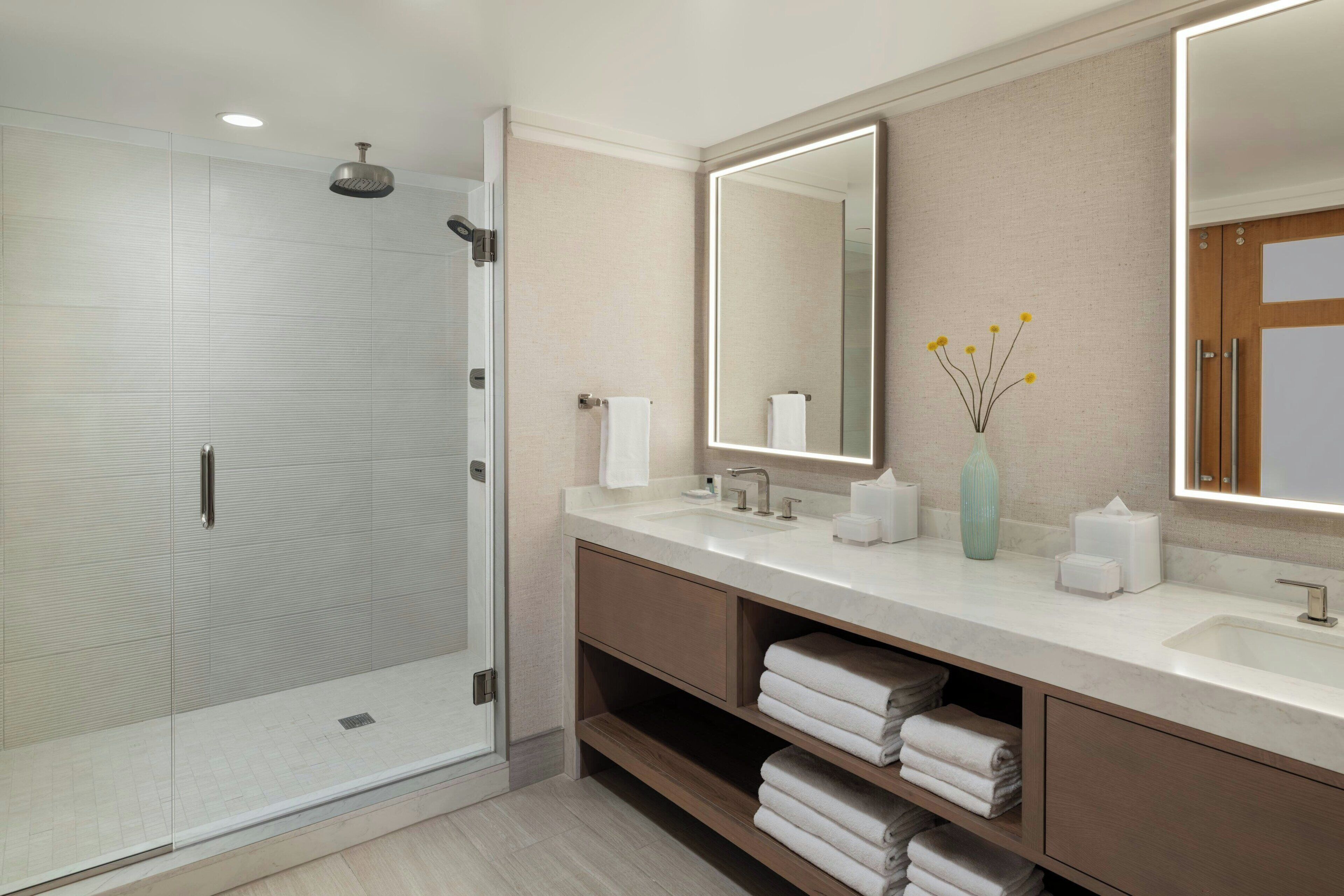 A modern bathroom with a glass shower enclosure, a large mirror, and a vanity with a sink and towel storage.