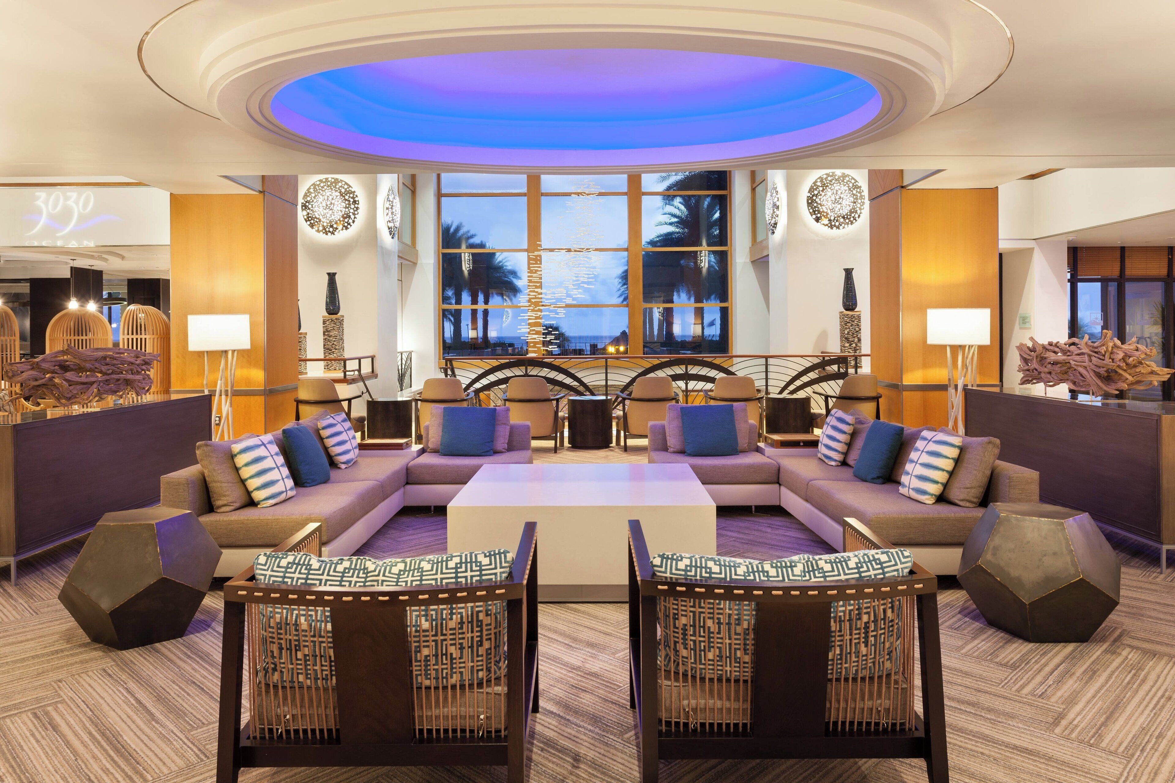 A modern lobby with a central seating area, large windows with a view, and a reception desk.