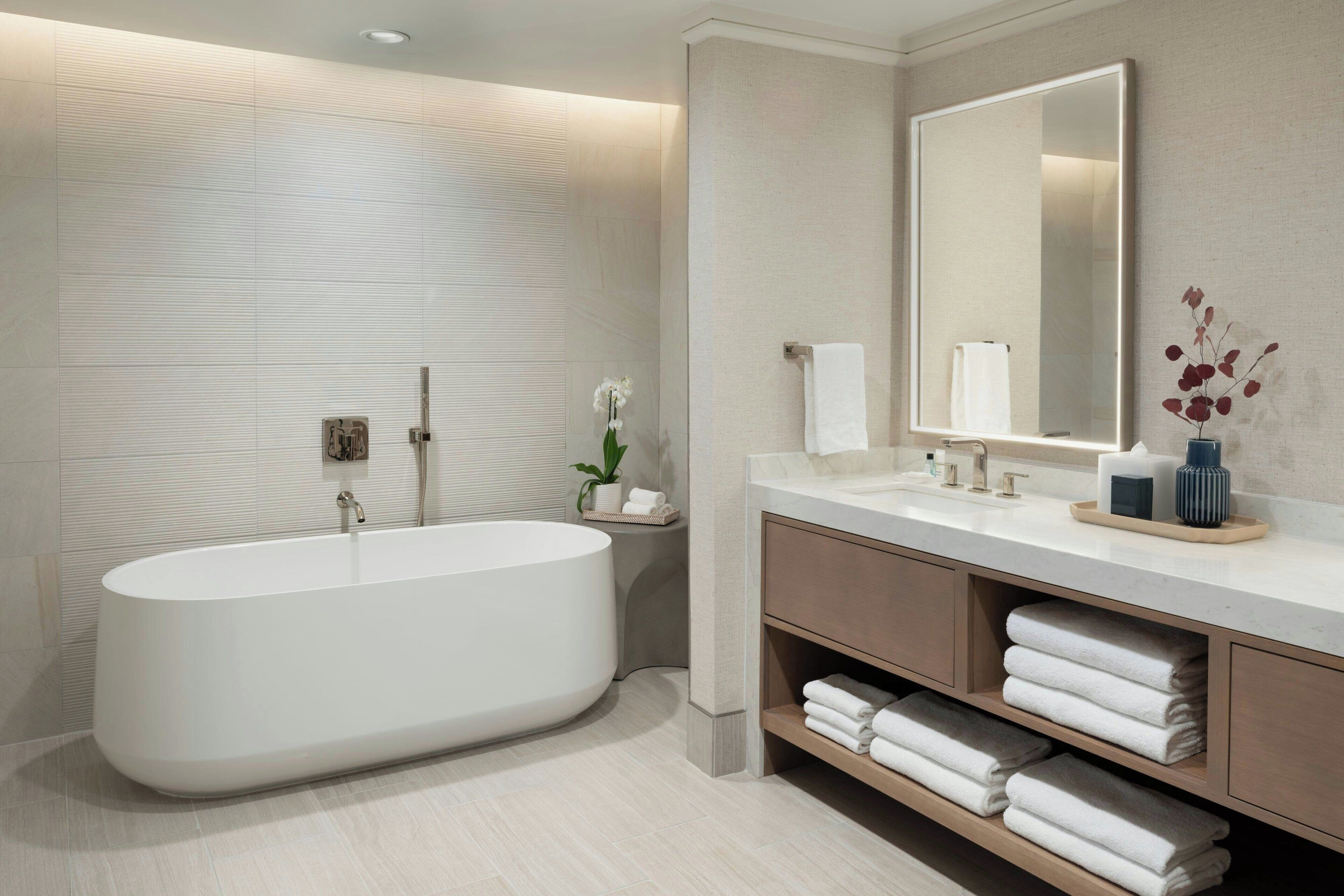 A modern bathroom with a freestanding bathtub, a large mirror, and a vanity with shelves for towels.