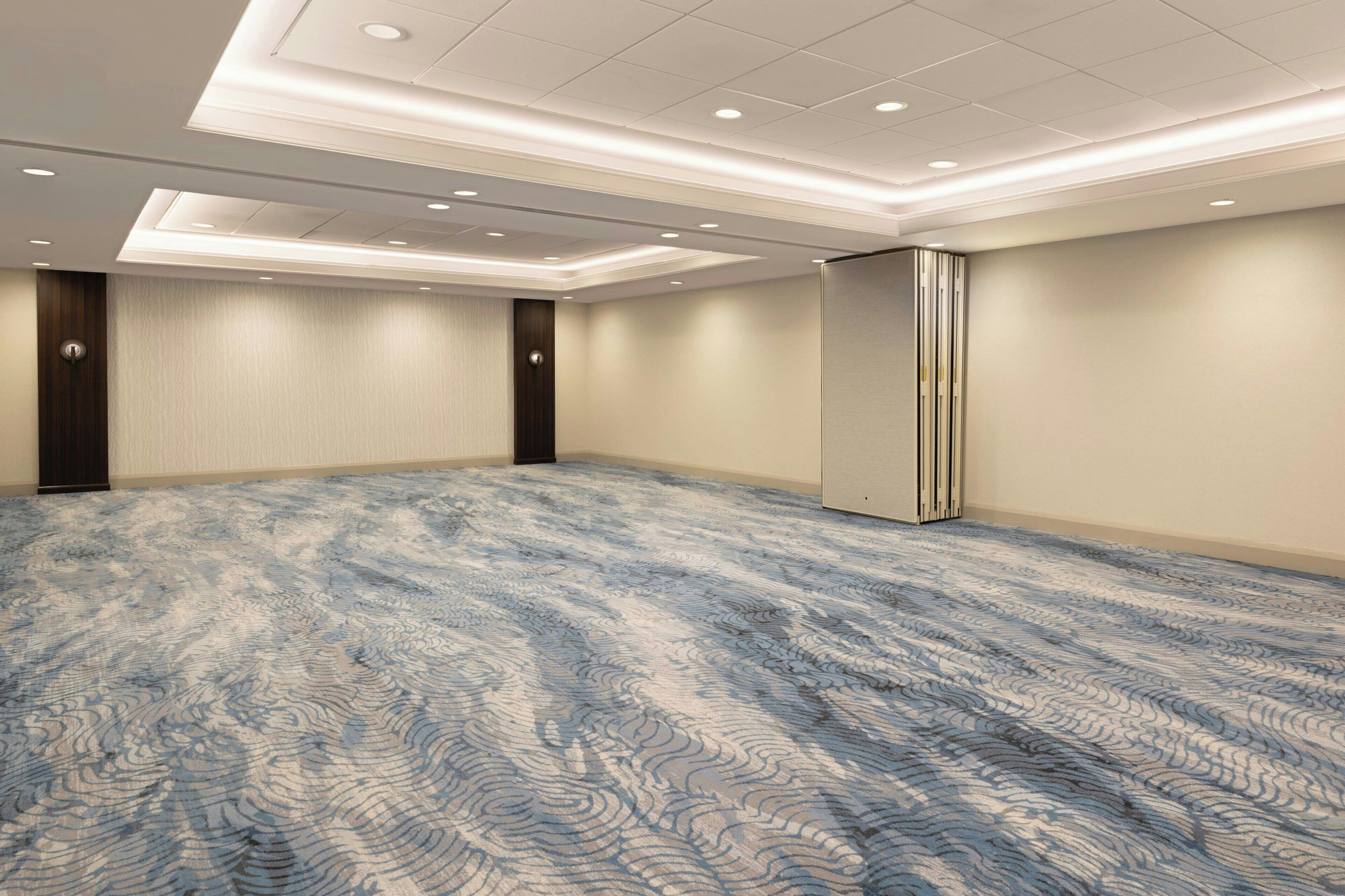 A conference room with a patterned carpet, recessed lighting, and a large whiteboard on the wall.