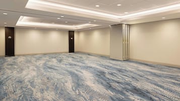 Un salón de conferencias con alfombra estampada, iluminación empotrada y una pizarra grande en la pared.