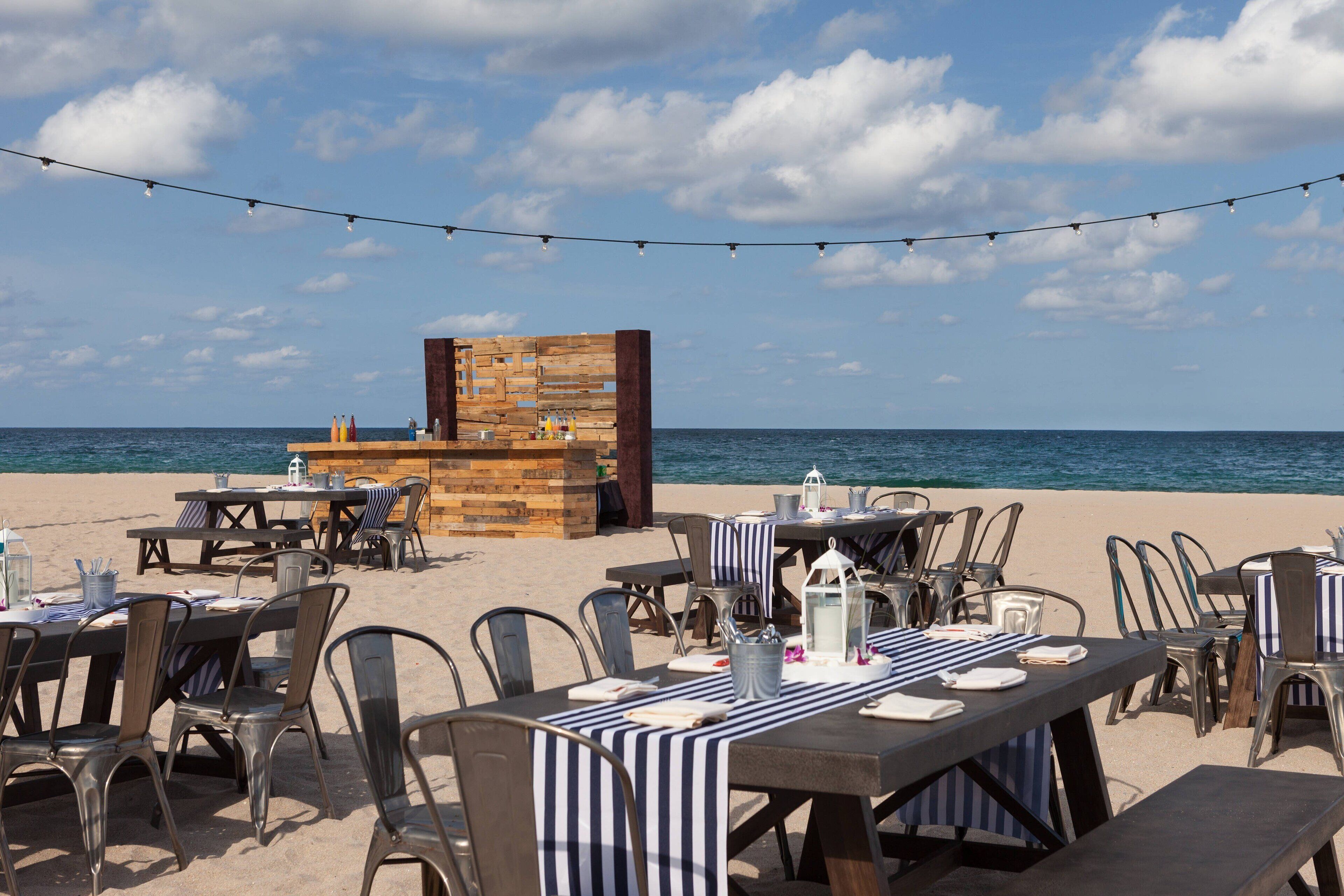 An outdoor dining area with tables and chairs, a wooden structure, and a view of the sea.