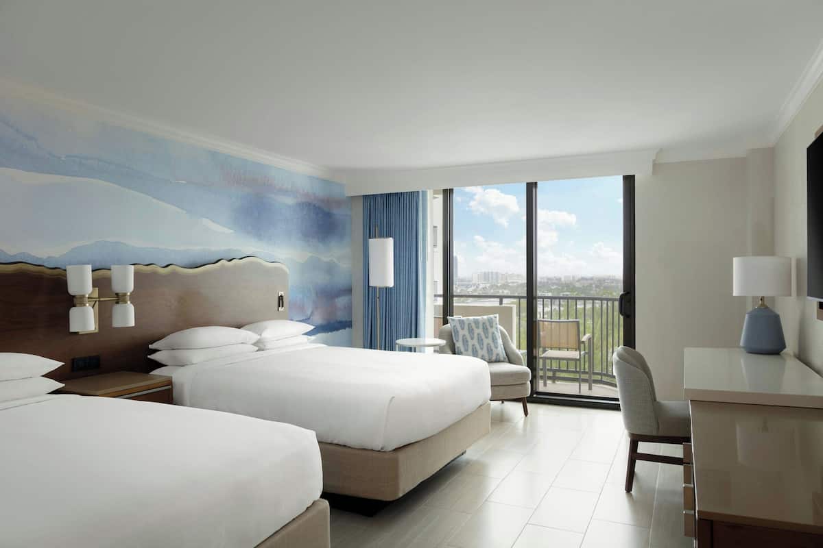 Een hotelkamer met twee bedden, een bureau en een balkon met uitzicht op de stad.