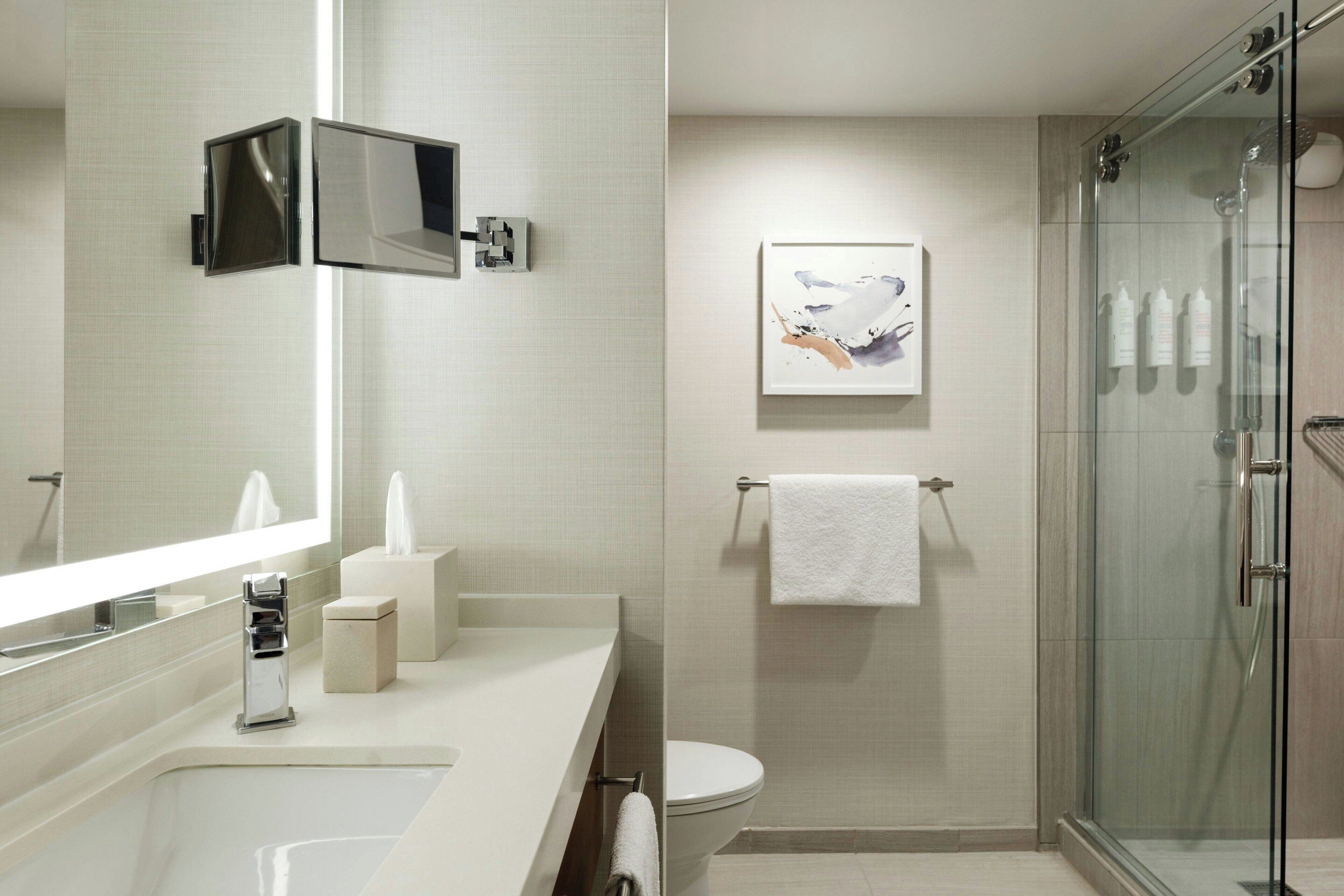 Un baño moderno con un espejo grande, un inodoro, cabina de ducha de vidrio y un perchero para toallas.