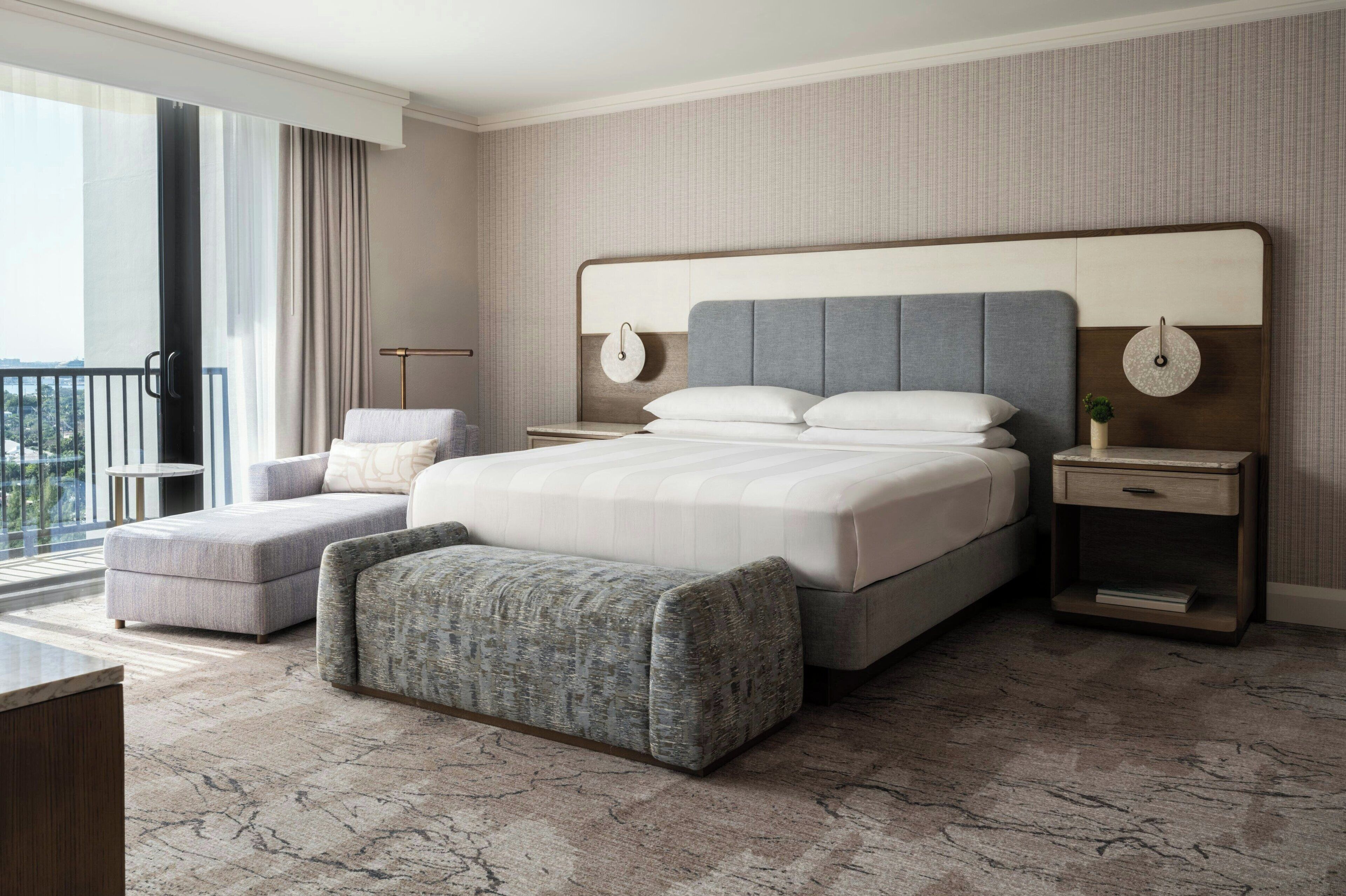 Una habitación de hotel moderna con una cama grande, una zona de estar y vistas al exterior.