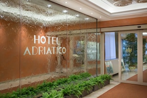 A hotel entrance with a glass wall displaying the name "HOTEL ADRIATICO".