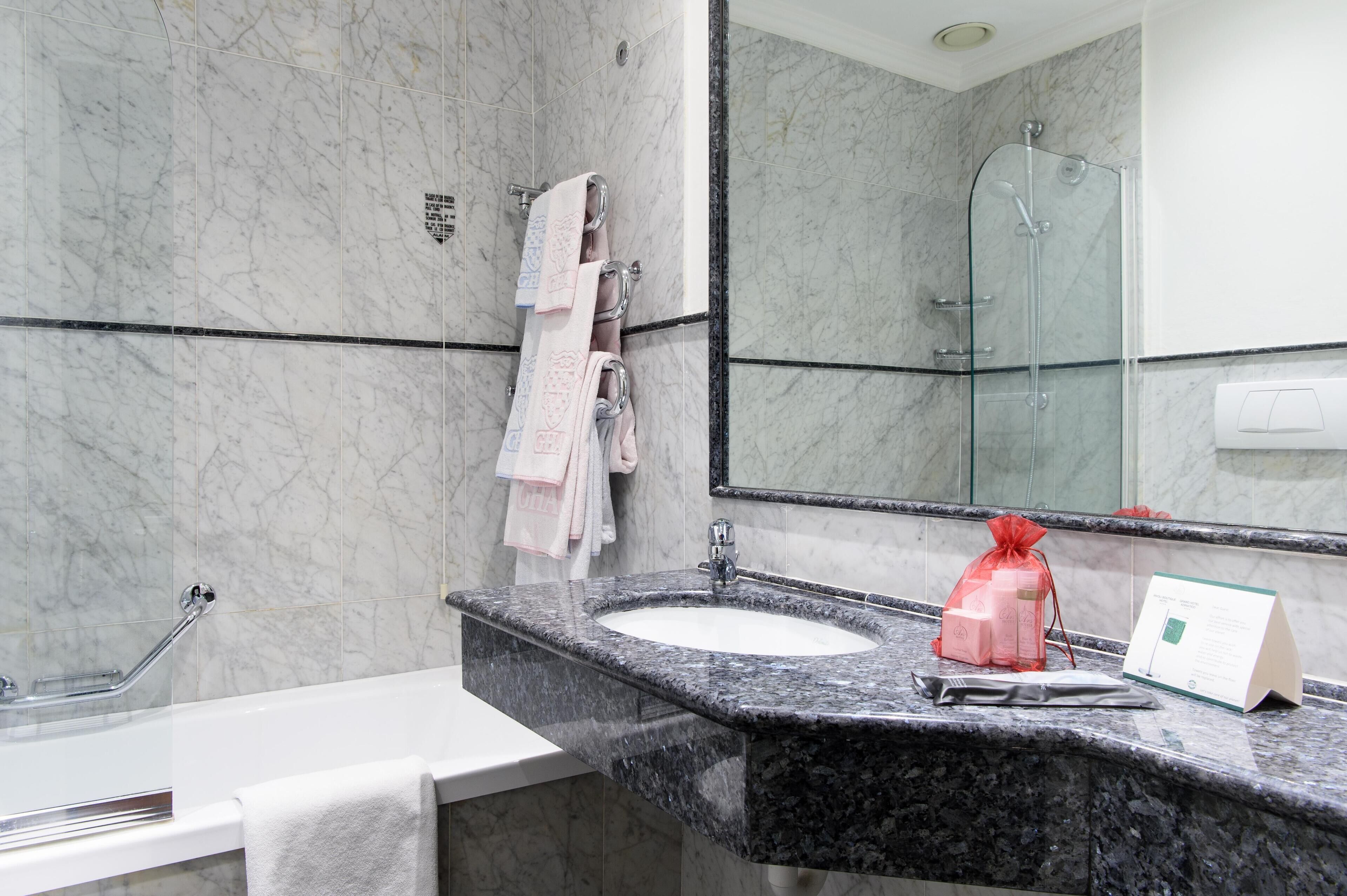 A bathroom with a marble wall, a glass shower enclosure, a sink with a marble countertop, and a towel rack with multiple towels.