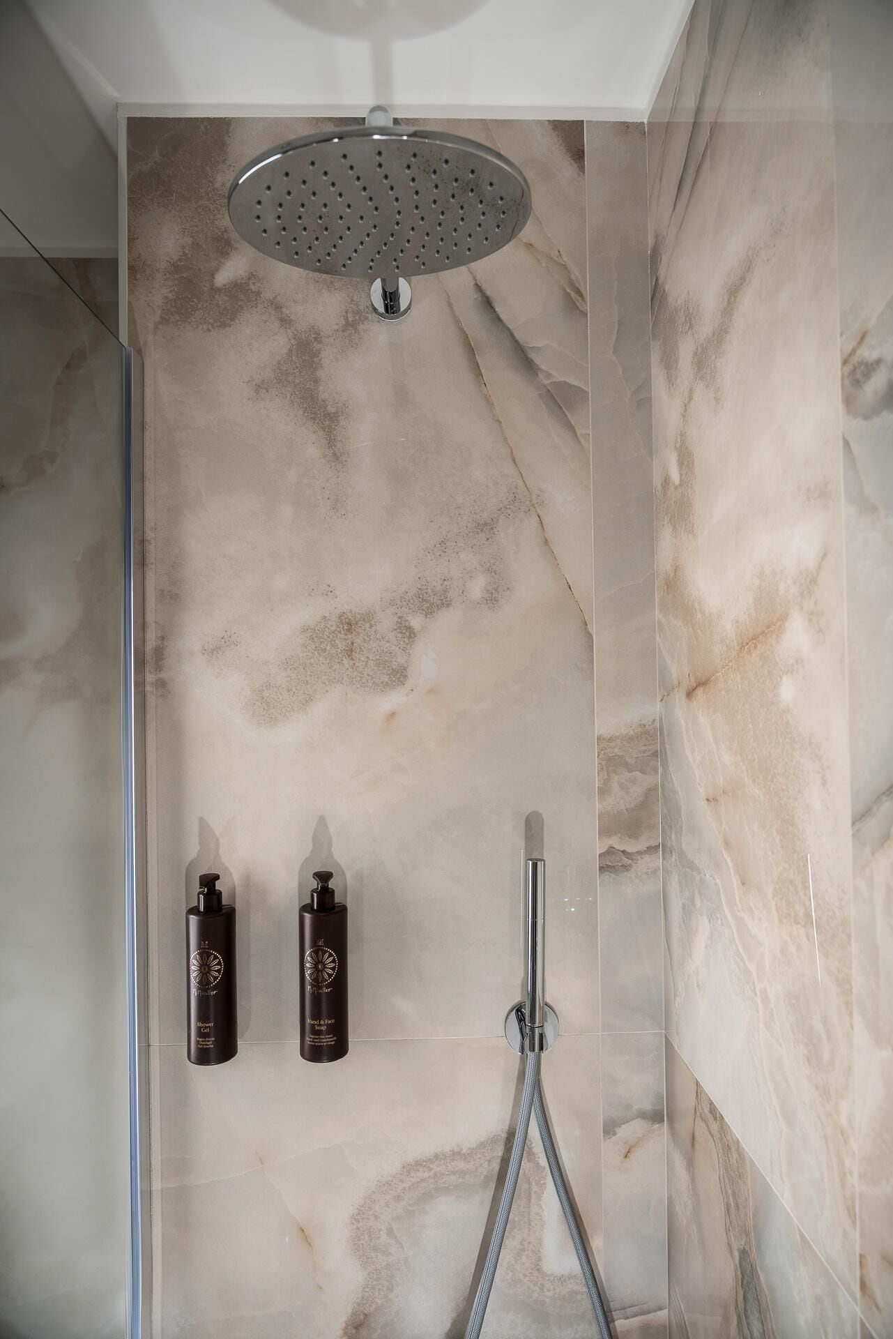 A modern shower with a rain showerhead, two bottles of shampoo and conditioner, and a handheld showerhead.