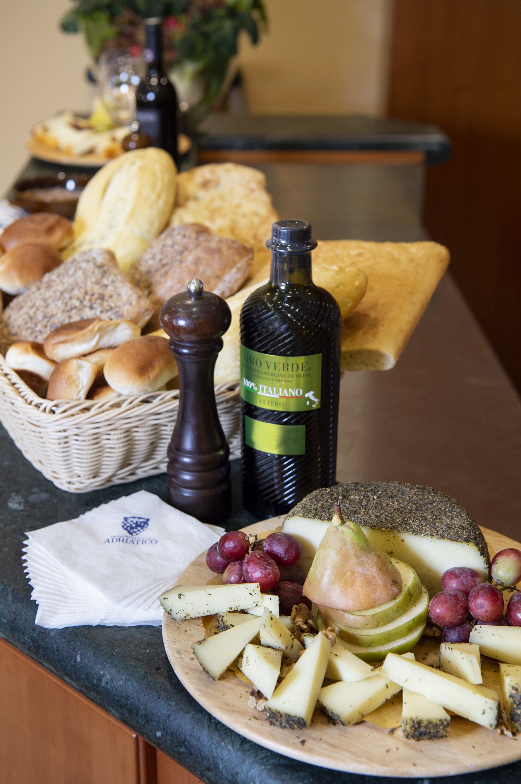 Een kaasplank met verschillende kazen, druiven en een peer, vergezeld van brood en een fles olijfolie.