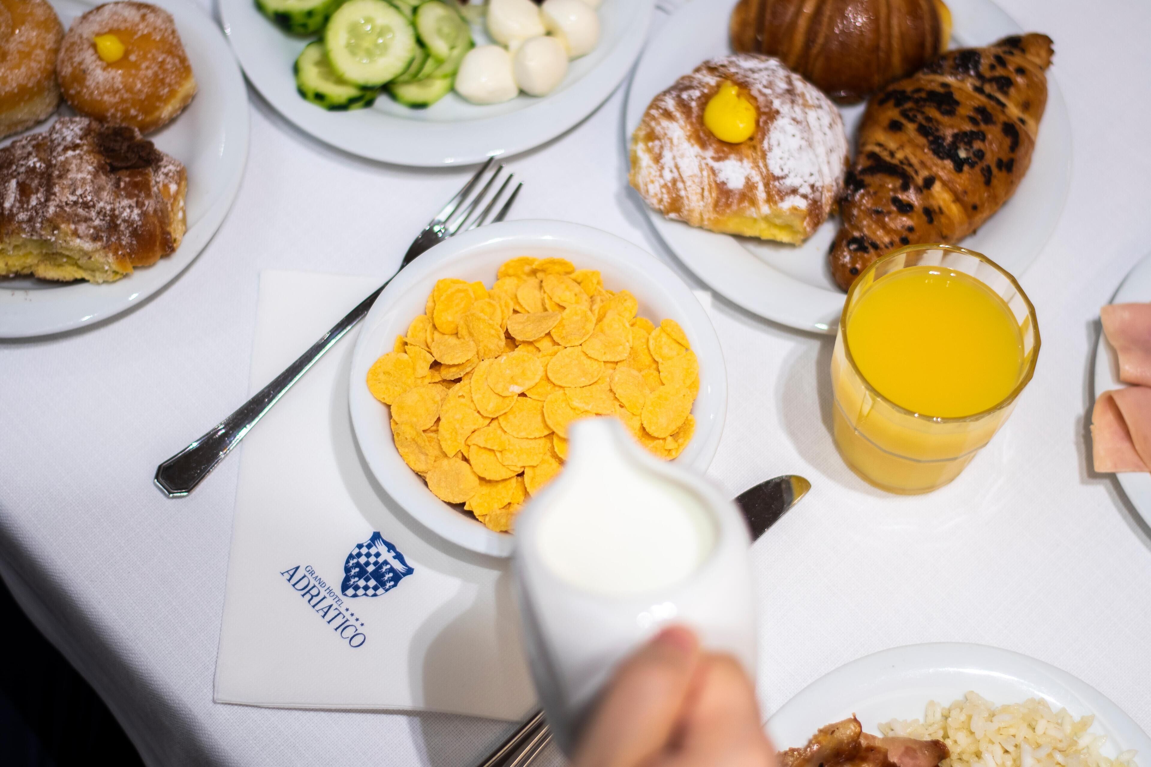 A breakfast table with plates of food, including croissants, a bowl of cereal, and a glass of orange juice.