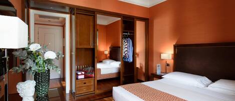 A hotel room with a large bed, a wardrobe, a mirror, a nightstand with a lamp, and a vase with flowers.