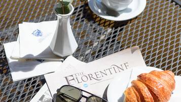 A table with a white vase, a cup and saucer, a croissant, sunglasses, and a magazine.