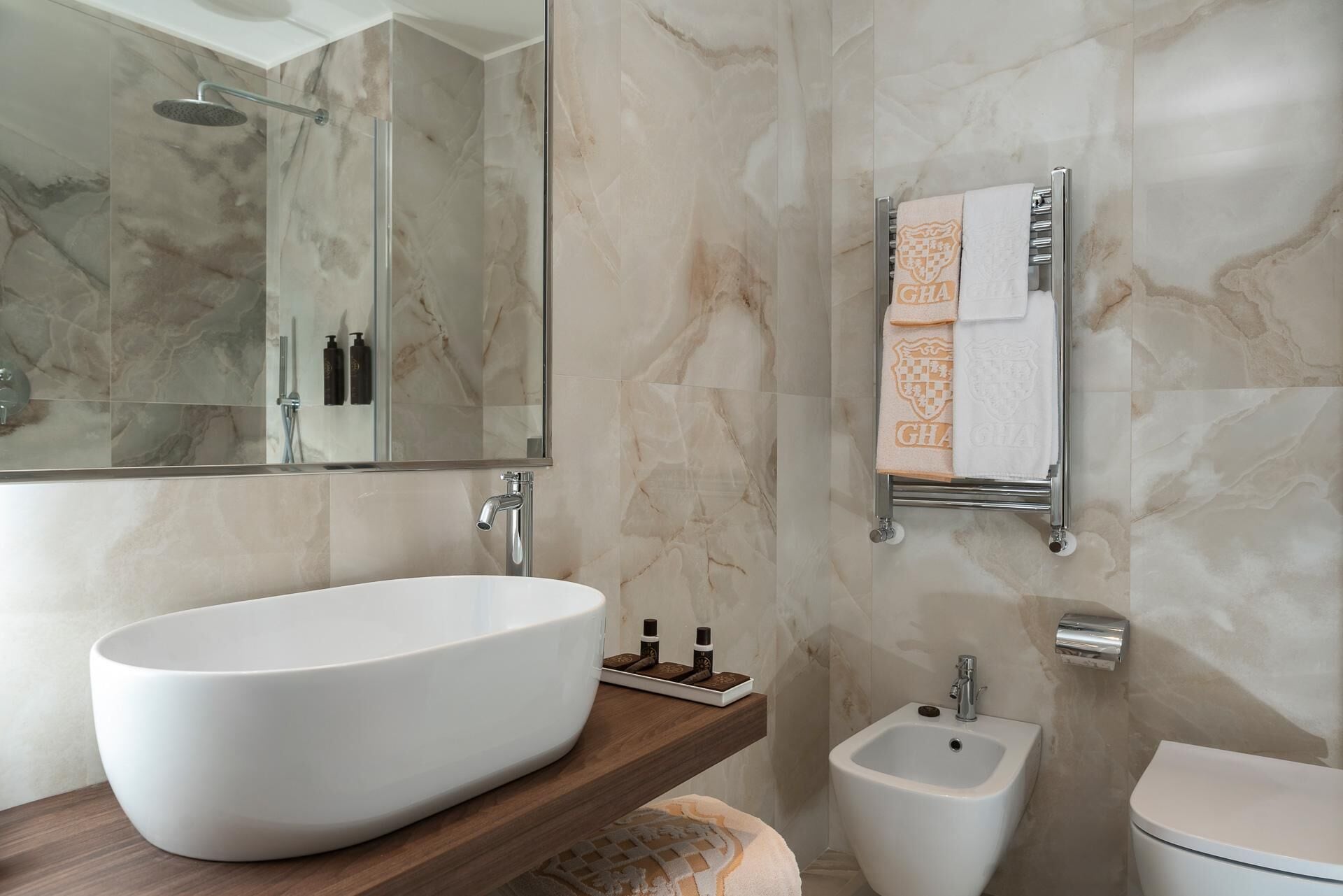 A modern bathroom with a large oval sink, a bidet, a toilet, and a mirror.