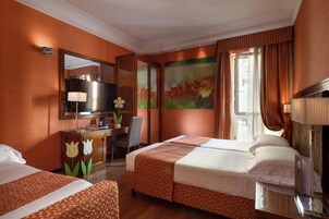 Habitación de hotel con dos camas, un escritorio con lámpara, un espejo y obras de arte en las paredes.