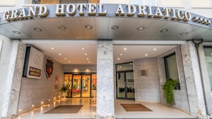 The entrance of Grand Hotel Adriatico with a marble facade, a large sign above the entrance, and a number '9' on a column. - Grand Hotel Adriatico (Florence)