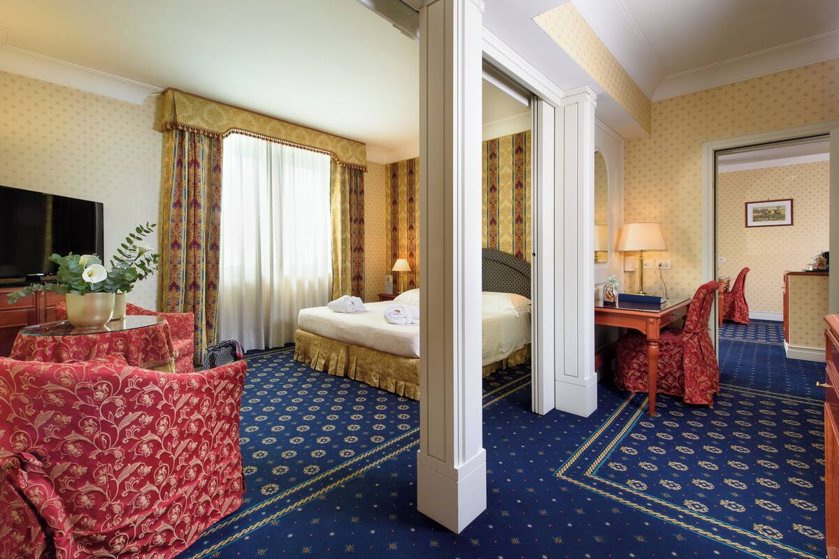 A hotel room with a bed, a desk, a television, a chair, and a table with a plant.
