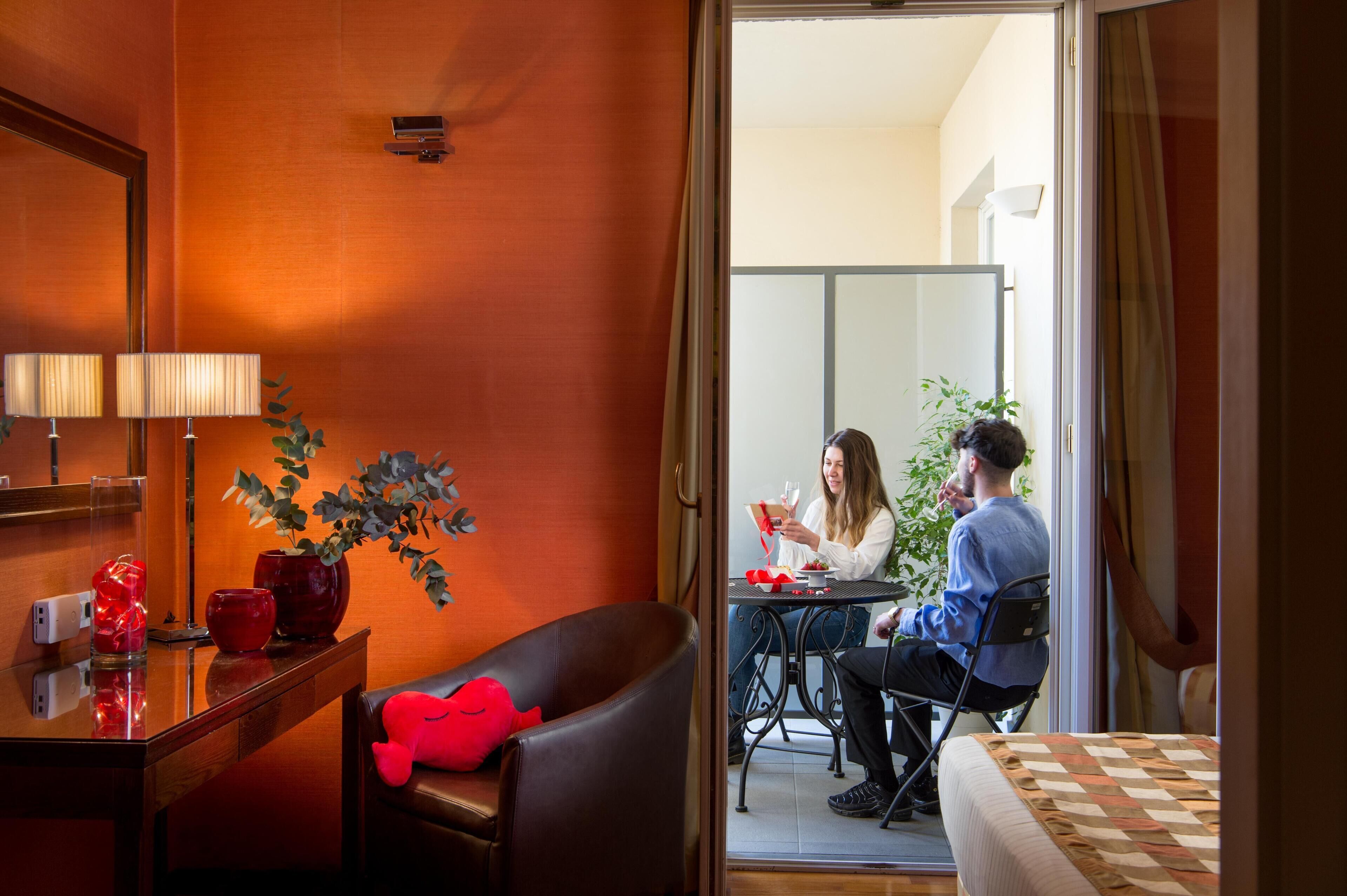 A hotel room with a dining area, a mirror, a red plush toy, and a plant.