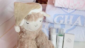A plush toy with a hat, a towel with 'GHA' text, and two bottles of lotion on a bed.