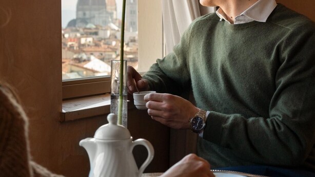 A person sitting at a table with a teapot and cups, a vase with a flower, and a view of a dome structure through a window. - Grand Hotel Adriatico (Florence)