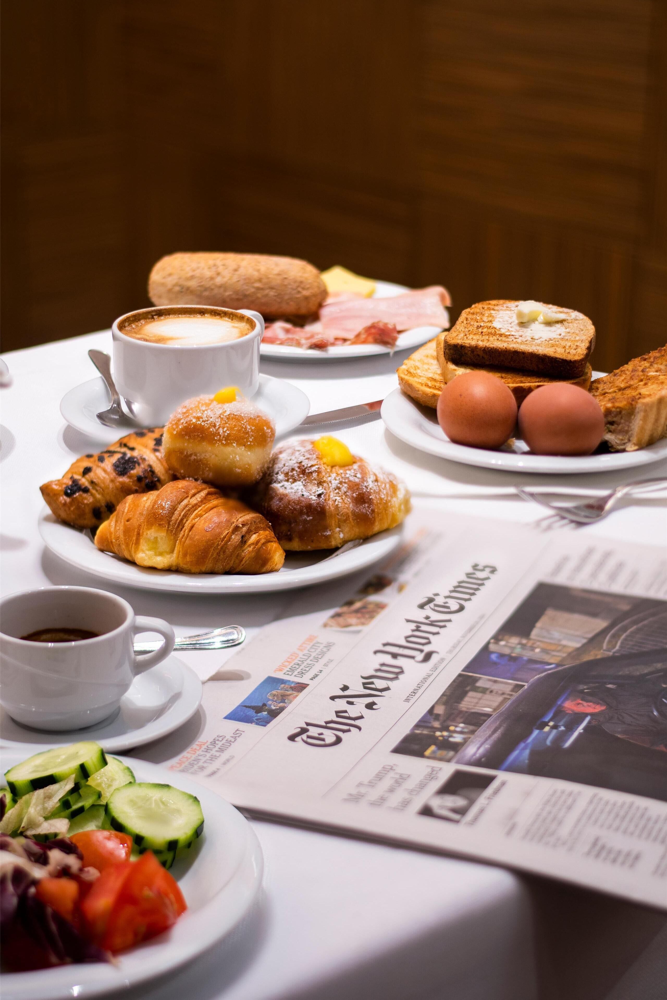 Une table de petit-déjeuner avec des croissants, du pain, des œufs et un journal.