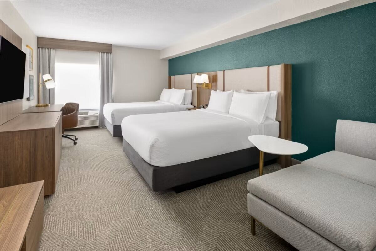 Ein Hotelzimmer mit zwei Betten, einem Schreibtisch, einem Stuhl und einem kleinen Tisch.