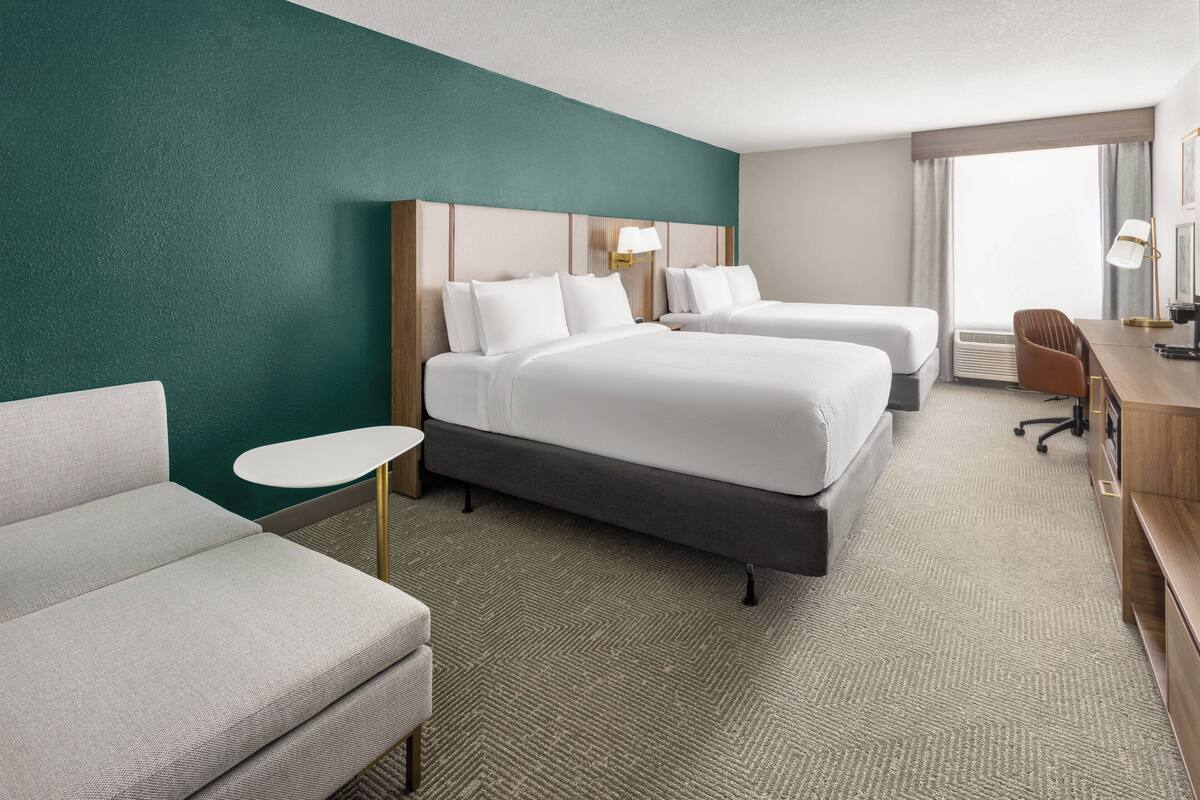 A hotel room with two beds, a desk, a chair, and a small table.