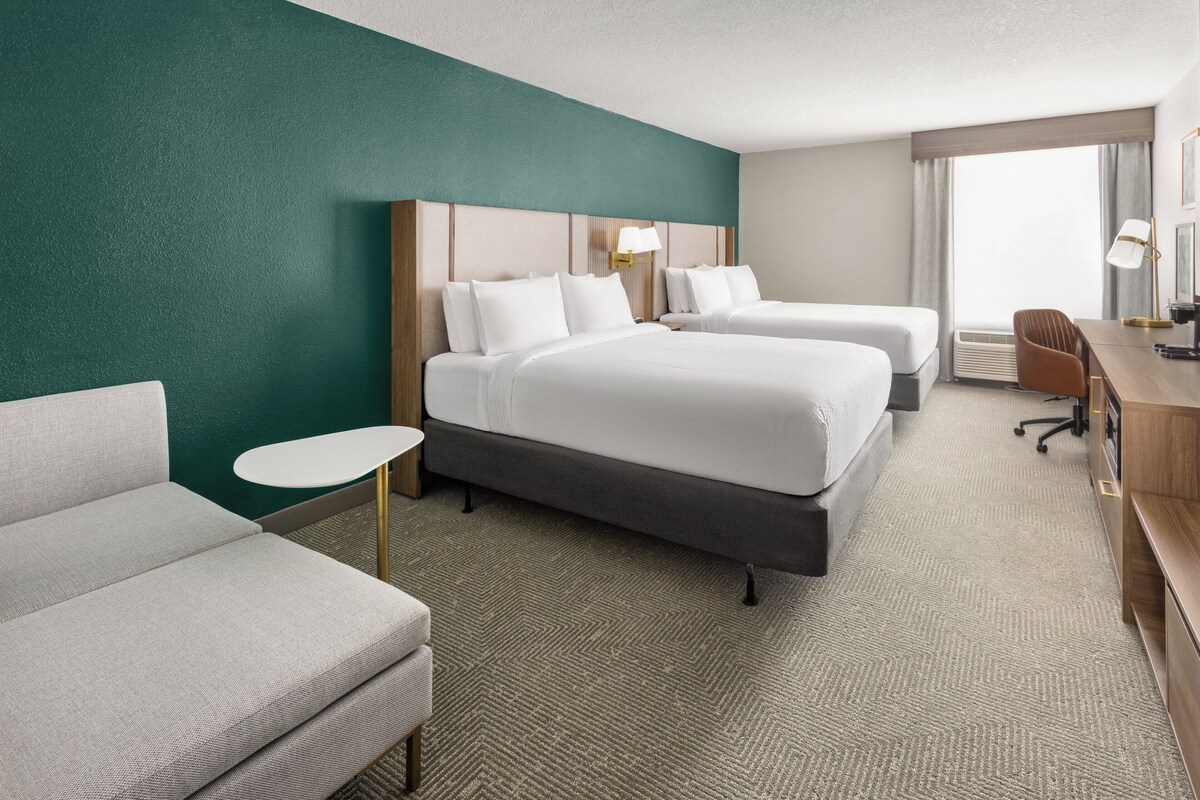 A hotel room with two beds, a desk, a chair, and a small table.