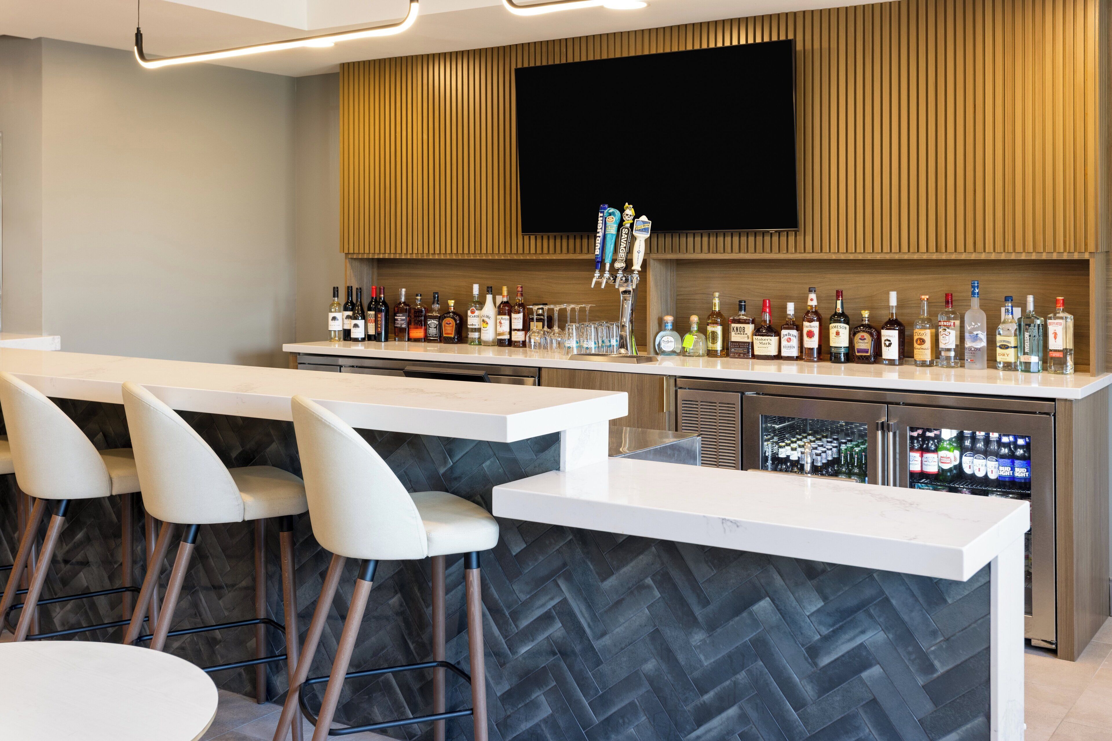 A bar area with a long counter, multiple stools, and a television mounted on the wall.