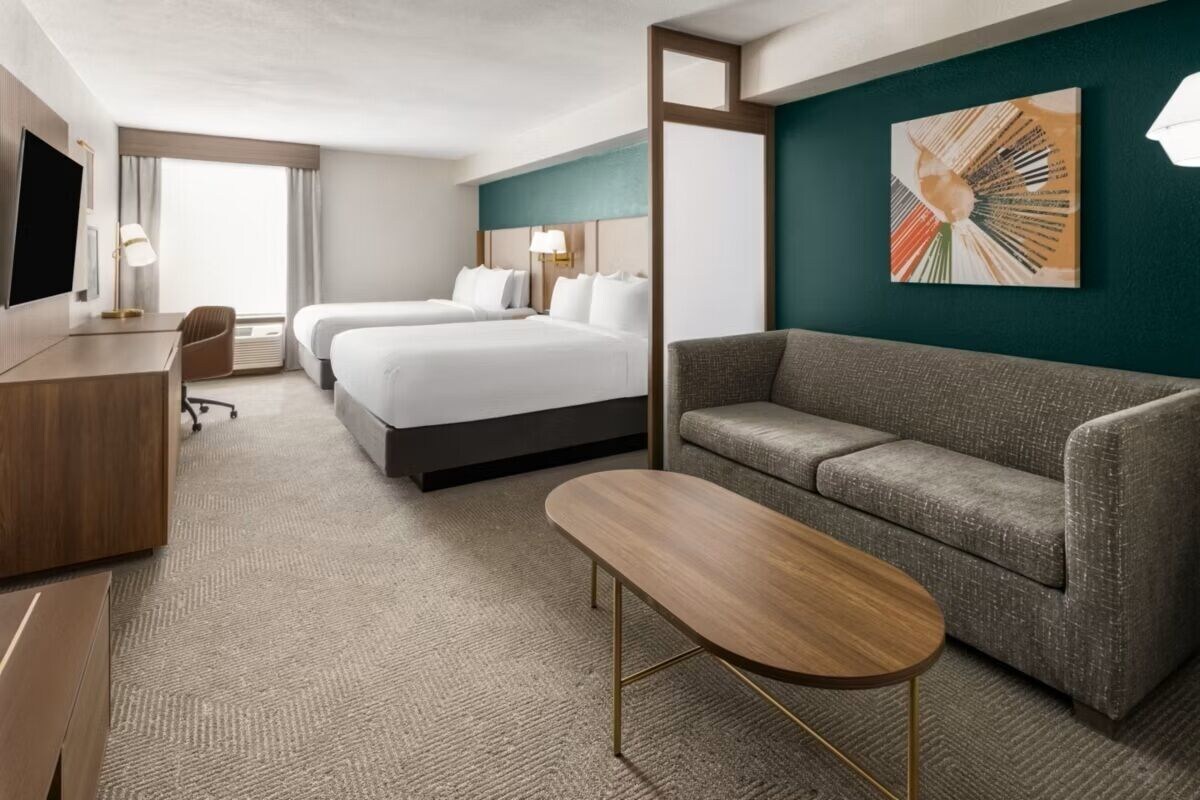 Ein Hotelzimmer mit zwei Betten, einem Schlafsofa, einem Schreibtisch und einem Fernseher.