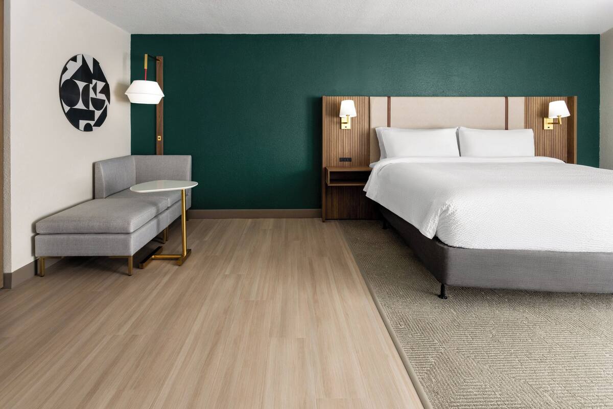 A hotel room with a bed, a gray sofa, a small table, and two wall-mounted lamps.