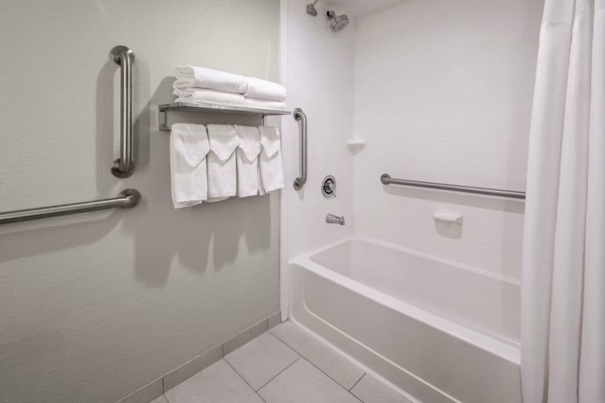 A bathroom with a white bathtub, grab bars, a towel rack with folded towels, and a shower curtain.