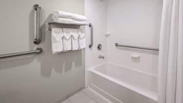 A bathroom with a white bathtub, grab bars, a towel rack with folded towels, and a shower curtain.