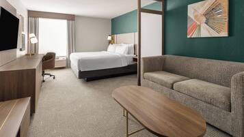 A hotel room with a bed, a sofa, a desk, a TV, and a painting on the wall.
