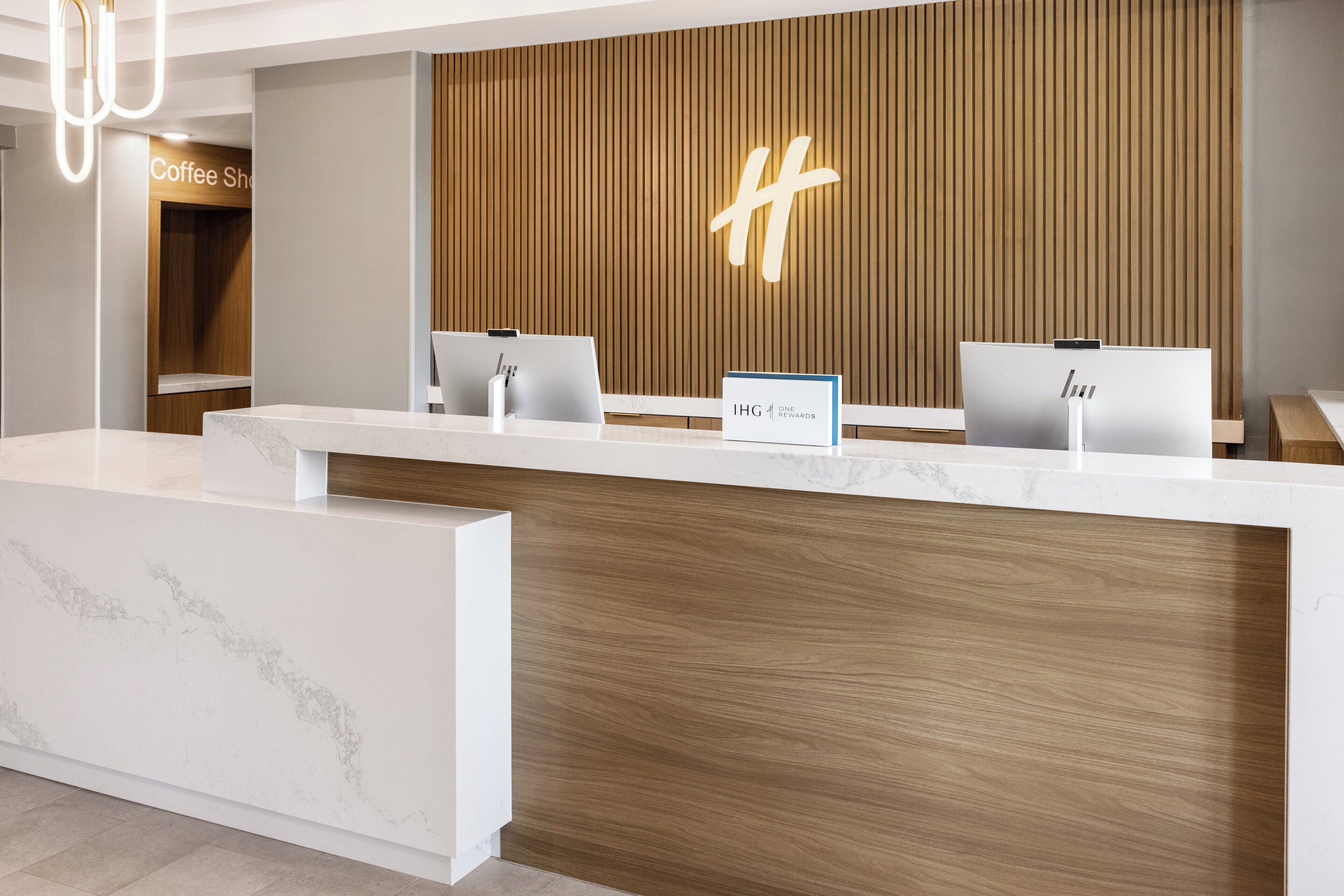 Een modern receptiebalie met een houten paneelwand en een groot, verlicht 'H'-bord.