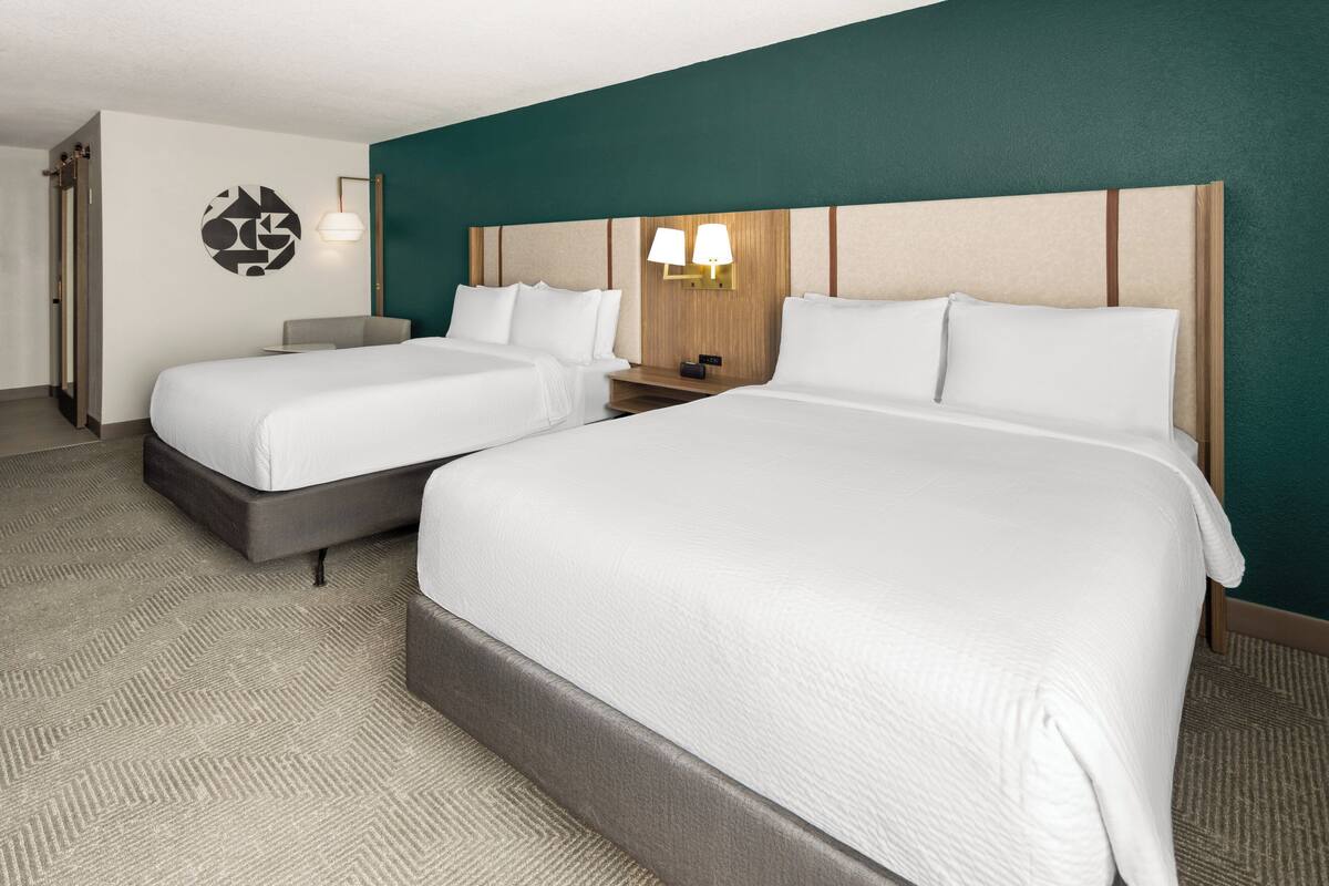 A hotel room with two beds, a wooden headboard, a wall-mounted lamp, and a carpeted floor.